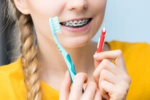 Young woman smiling cleaning and brushing teeth with braces using toothbrush