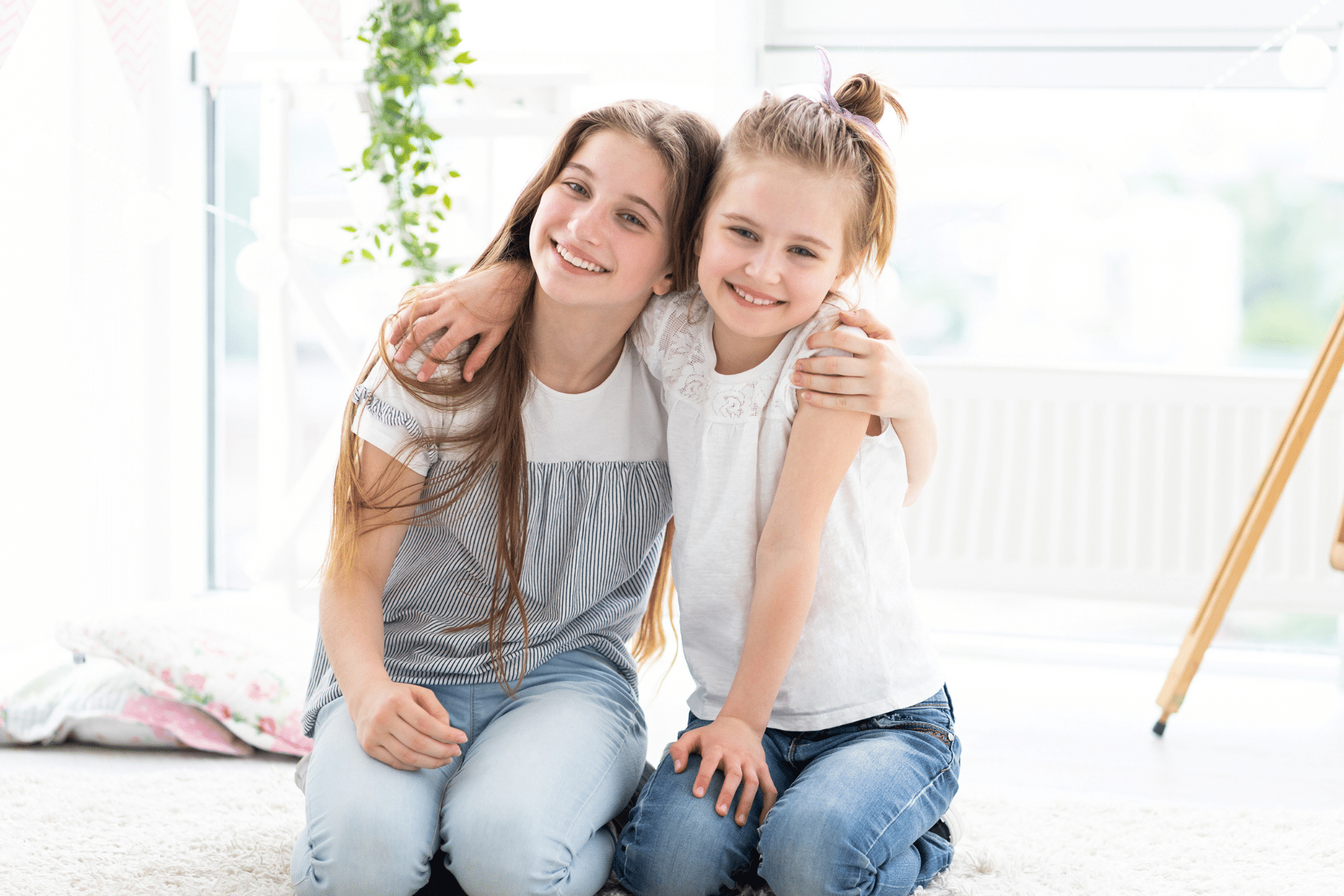 Two smiling young girls hugging while sitting indoors