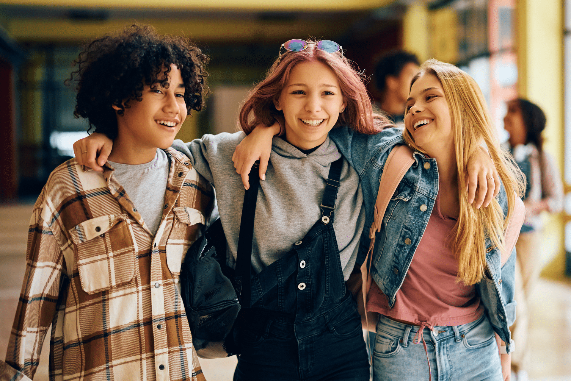 Group of three happy teenagers walking down a school hallway