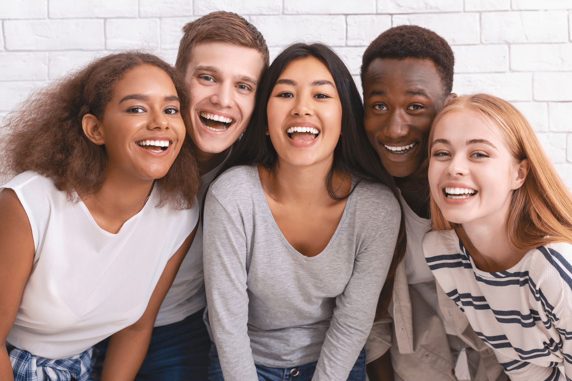 Five smiling young adults posing together against a white brick wall