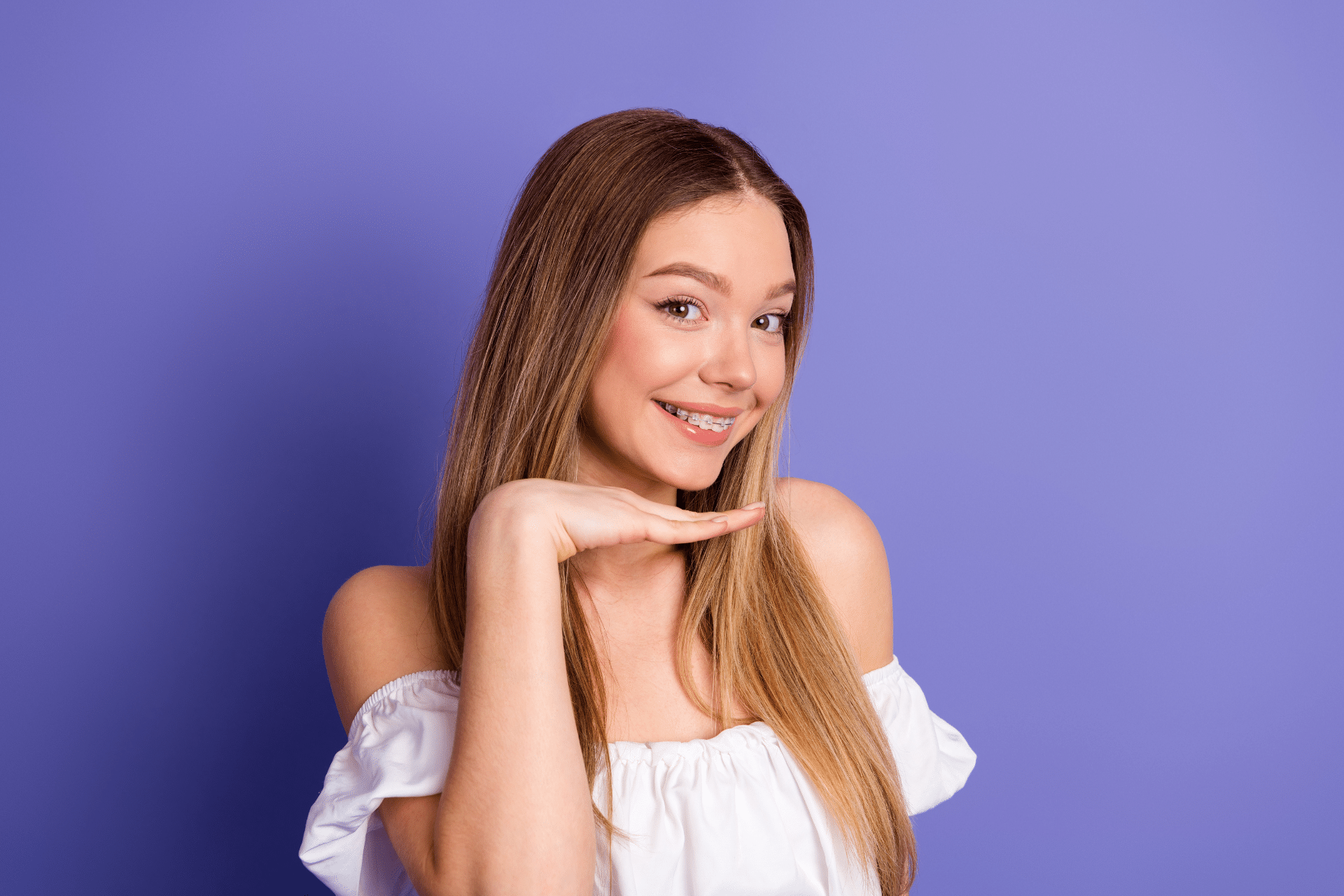 Young woman smiling with clear braces against a purple background.